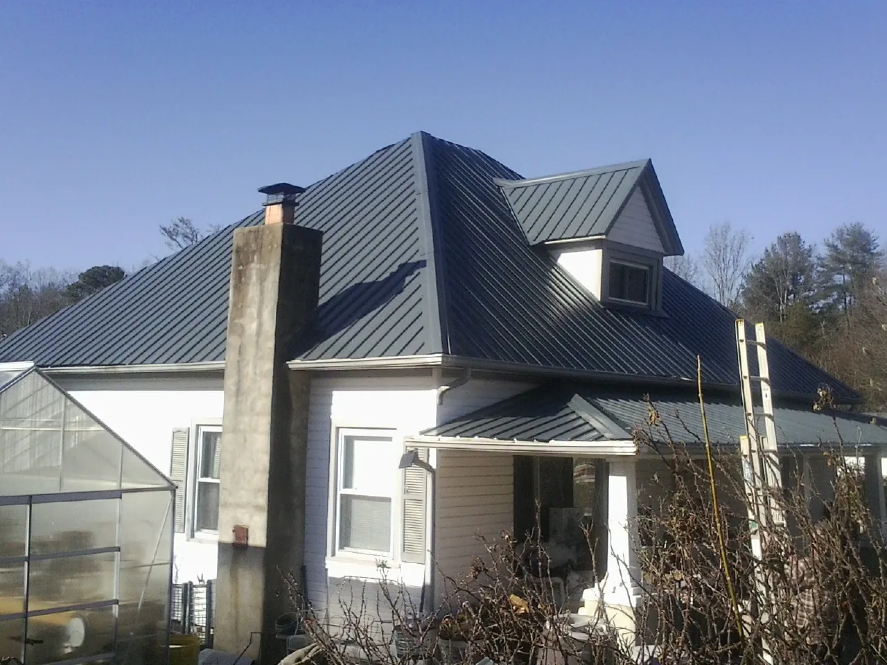 Dark blue standing seam metal roof on a white farmhouse with dormer — Slate & Tile Roof Repair by Roofing Brothers in Ronan