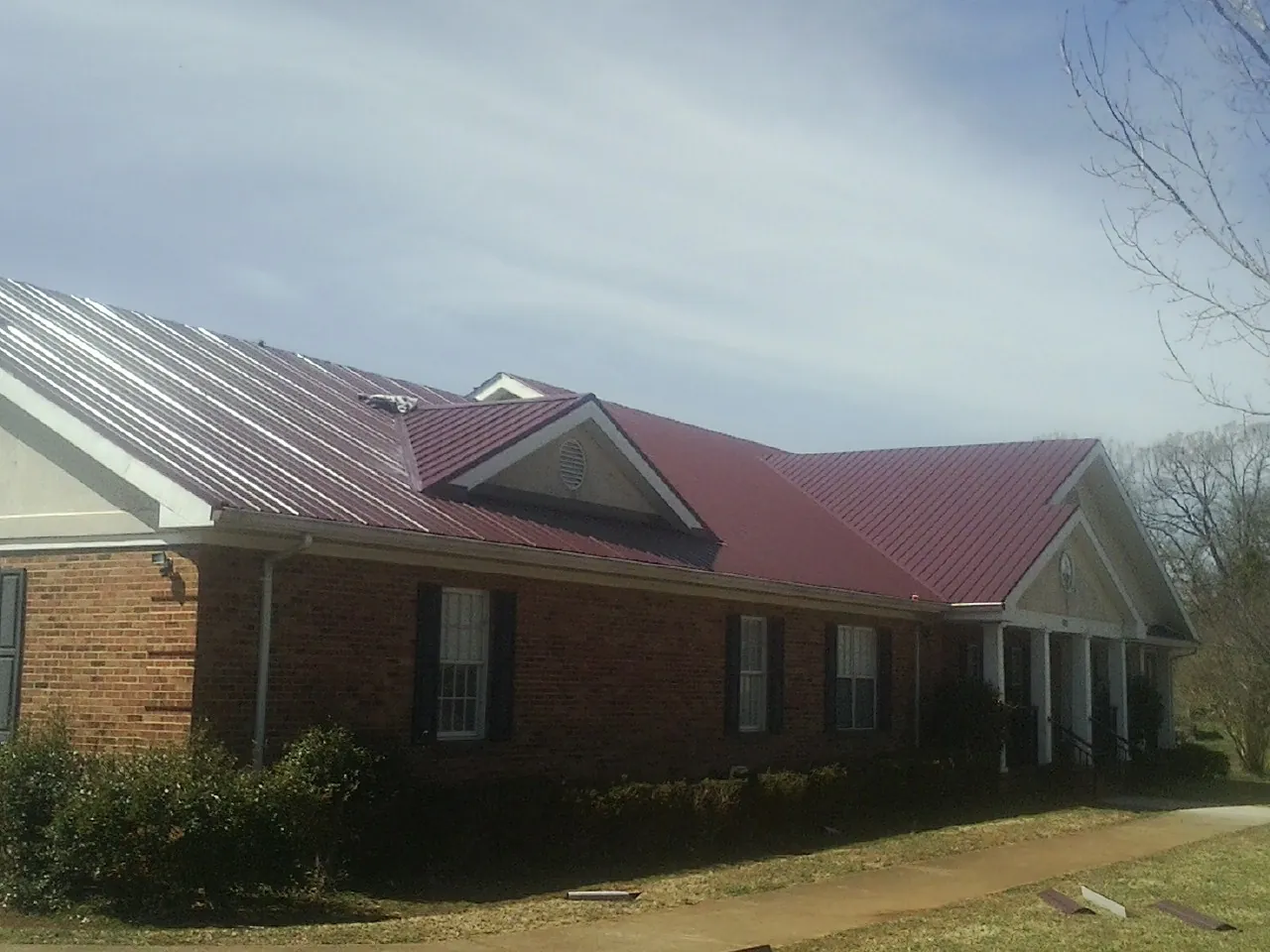 Red metal roof with gabled entries on a long brick building, from a Hail Damage Roof Repair job in Ronan