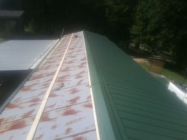 Old rusted panels beside newly installed green metal roofing — Wind Damage Roof Repair by Roofing Brothers in Ronan