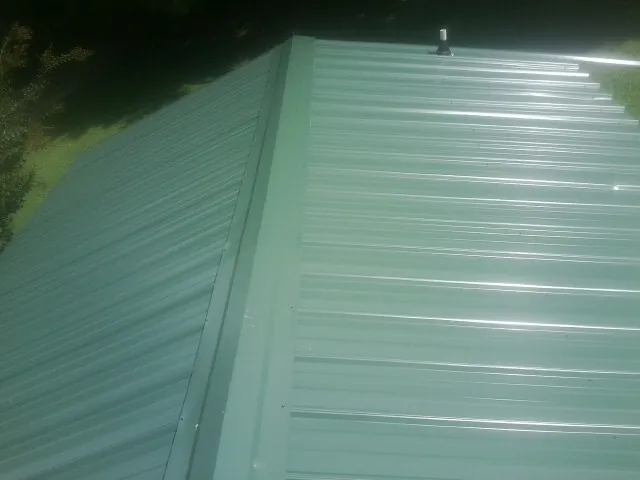 New green metal panels meeting at the ridge of a roof — Flat Roof Repair work by our crew in Ronan