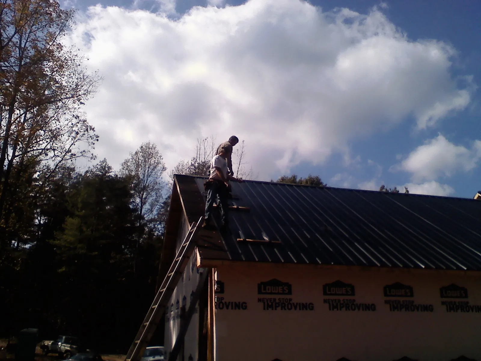 Roofer fastening dark metal panels high against a cloudy sky, from a Roof Inspection job in Ronan