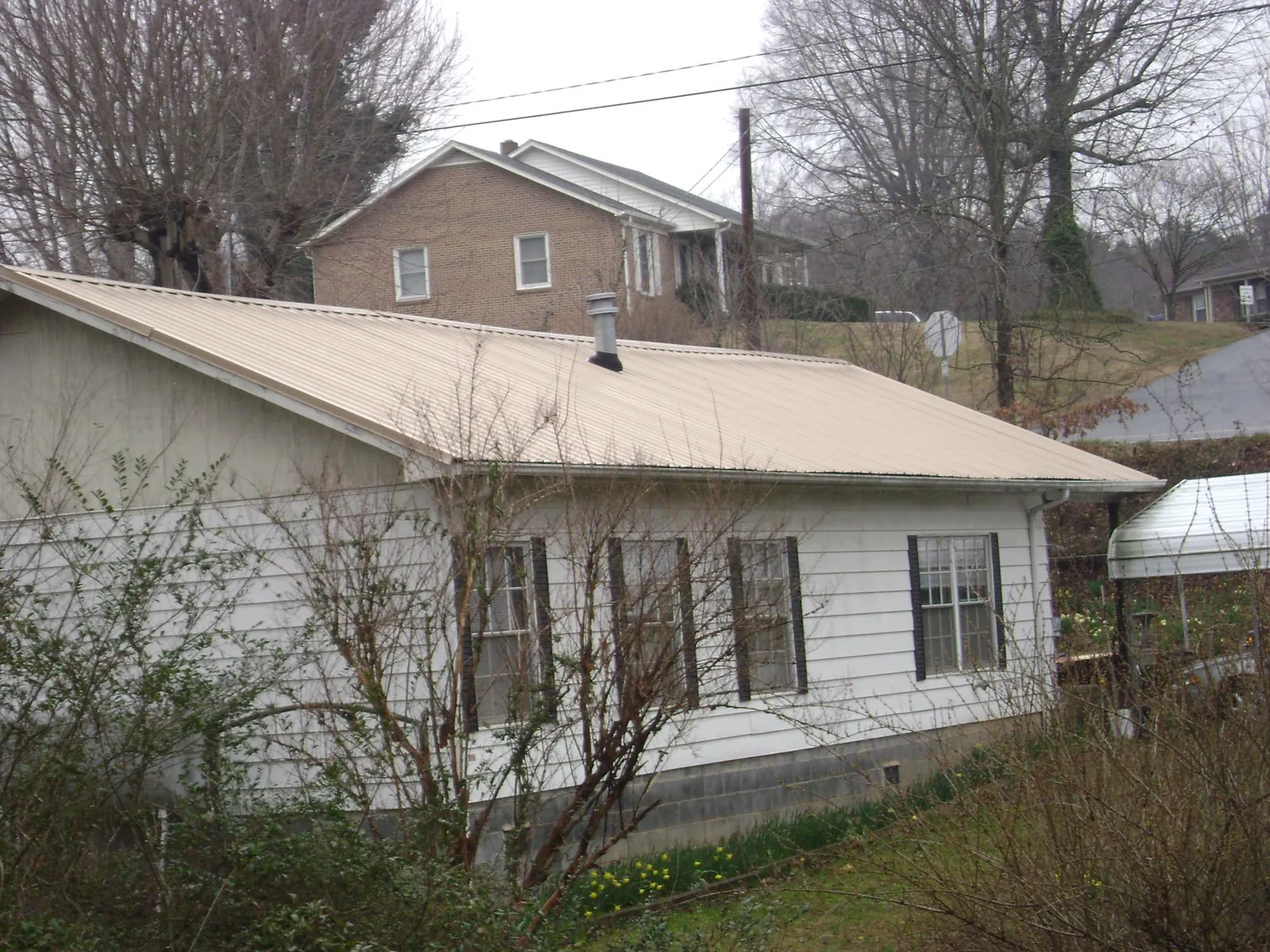 Tan metal roof on a white sided house set into a hillside — Commercial Roofing by Roofing Brothers in Ronan