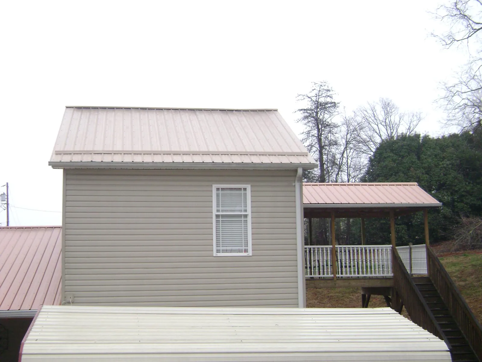 Tan metal roofs on a two story addition and attached porch, from a Roof Replacement job in Ronan